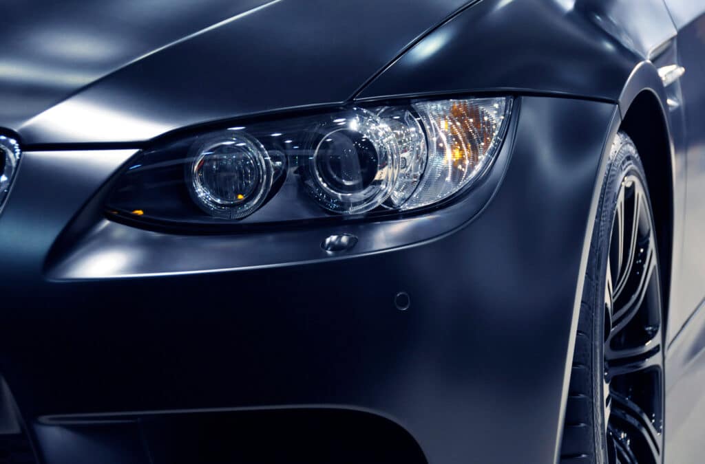 Phare BMW Sport Matte : Gros Plan Design et Jantes Gros plan sur le phare avant gauche d'une BMW sport sombre, finition mate, avec anneaux lumineux et clignotant ambré, et une partie de la roue.