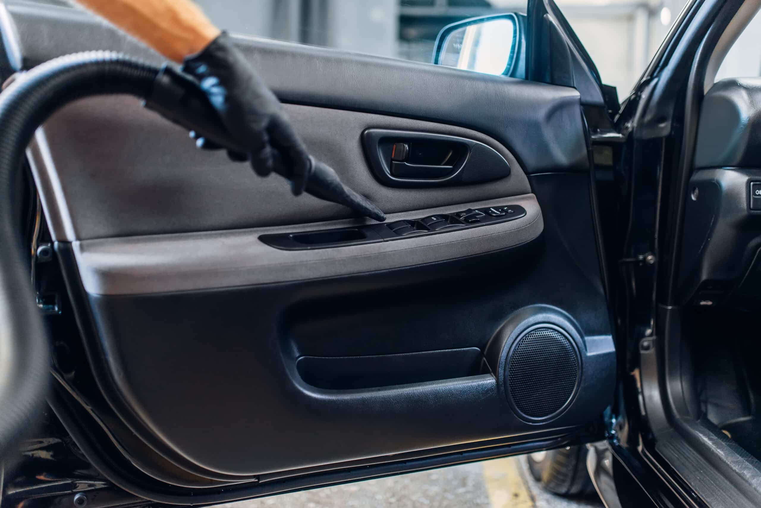 Main gantée de noir aspirateur la console de commande de la portière intérieure d'une voiture, près des commandes des vitres "AUTO" et "MIRROR".