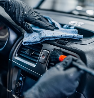 Lavage voiture haute pression : mousse et eau sur carrosserie Voiture foncée lavée avec un nettoyeur haute pression, de la mousse blanche recouvrant le capot et le pare-brise, sol mouillé.