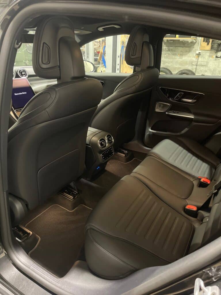 Intérieur Mercedes-Benz luxe : sièges arrière cuir noir. Sièges arrière en cuir noir d'une Mercedes-Benz. Console centrale avec aérations turbines, commandes de climatisation et écran MBUX affichant 'Mercedes-Benz'.